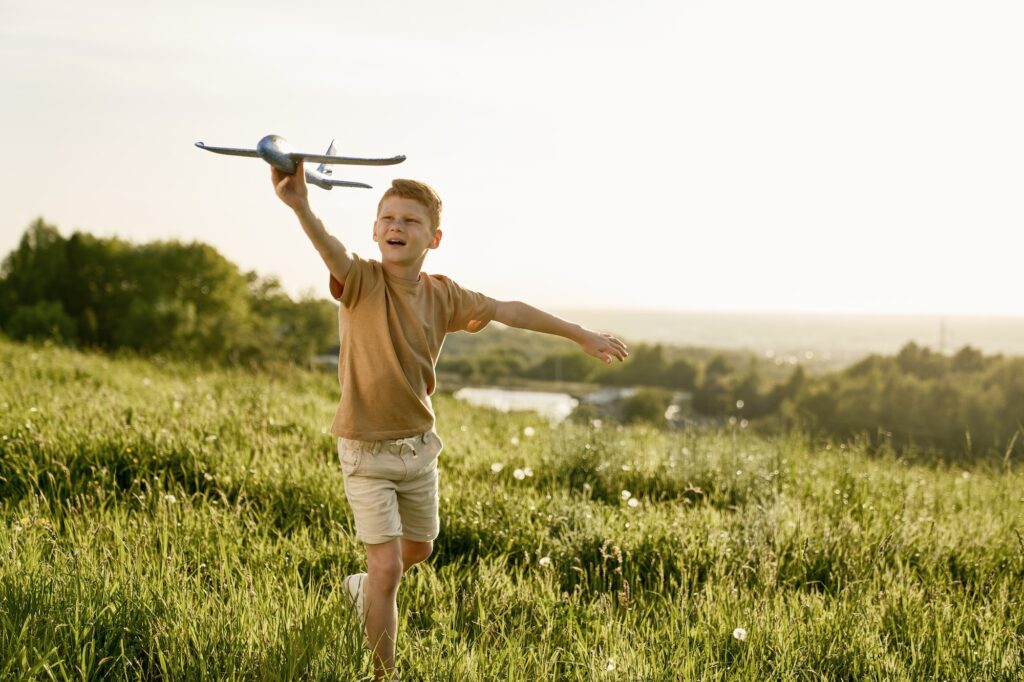 Ginger boy playing toy airplane on the meadow