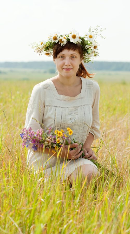 Sitting girl with flowers posy in summer field