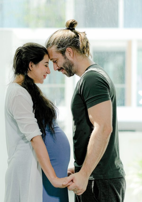 Man and pregnant woman stand in front of glass window of their house